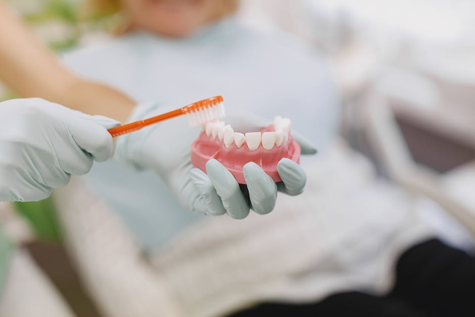 Close-up of hands in gloves demonstrating proper tooth brushing technique using a dental model.
