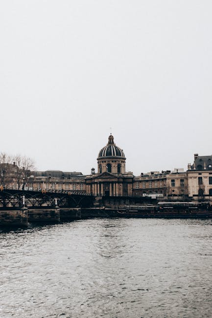 Aged institute facade with columns against bridge above Seine River under light sky in Paris France